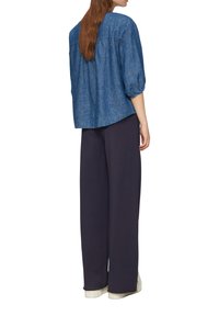 Blauwe denim top met een ronde halslijn en pofmouwen, gecombineerd met loszittende marineblauwe broeken en witte sneakers.