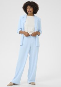 Light blue blazer with matching wide-leg trousers, layered over a textured cream top. The fabric appears smooth; shoes are light-colored flats.