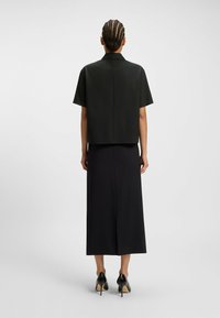 Black cropped shirt with short sleeves, paired with a long black skirt. Smooth fabric, simple design, and a back slit detail on the skirt.
