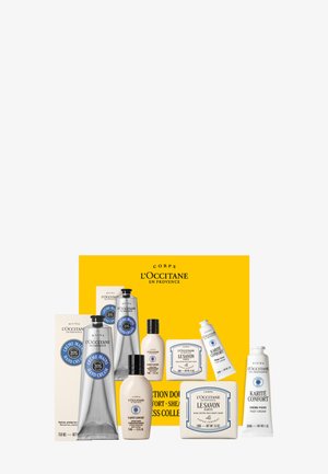 L'Occitane hand cream, body lotion, soap bars, and foot cream arranged in front of a yellow box with brand name.
