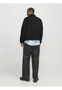 Veste en cuir noir, chemise à rayures bleues en dessous, jeans foncés, bottes noires. Design simple, couture visible, coupe décontractée.