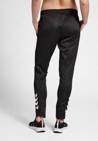 Melnas sporta bikses ar slim fit, elastīgu jostu, rāvējpogu potītēm un baltu ševronu rakstu detaļām sānos.