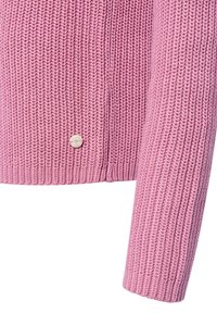 Close-up van een roze dikke ribgebreide sweatermouw en onderzoom met een kleine ronde beige logo-knop bevestigd.