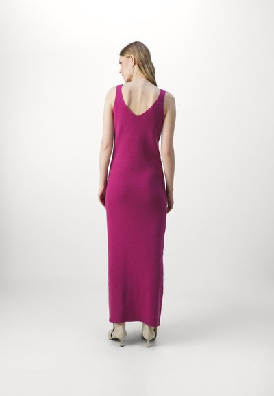 Robe maxi en tricot fuchsia avec un dos en V et de larges bretelles. Le tissu semble lisse et ajusté, s'étendant jusqu'aux chevilles.