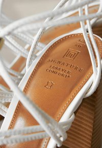 Hvide stroppesandaler med en brun læderindersål præsenteret med "SIGNATURE" og "FOREVER COMFORT", struktureret træhæl. Størrelse 40.