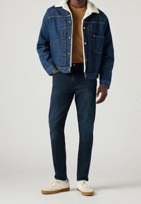 Džínová bunda s umělým ovčím límcem v tmavě modré barvě, zkombinovaná s tmavě modrými slim-fit džíny a krémovými teniskami se světlými hnědými podrážkami.