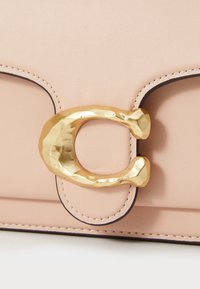 Blush leather bag featuring a hammered gold-tone clasp, contrast stitching, and a smooth texture. Compact design with rounded accents.