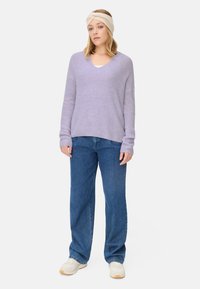 Hellblauer, gerippter Strickpullover mit V-Ausschnitt, kombiniert mit blauen Straight-Leg-Jeans und cremefarbenen Sneakers, ergänzt durch ein beigefarbenes Haarband.