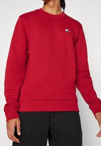 Sudadera roja hecha de una mezcla de algodón, con cuello redondo, puños acanalados y un pequeño parche con logo en el pecho.