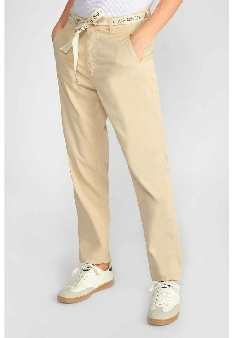 Beige broek met een relaxte pasvorm, voorzien van een strikceintuur met tekstdetail, zijzakken en een zachte katoenen stof. Gemaakt in combinatie met witte sneakers.
