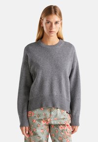Pull en tricot gris avec un col rond et un ourlet côtelé. Il présente des manches longues et une coupe décontractée, associé à un pantalon à motif floral.