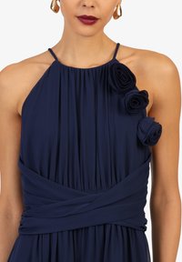 Navyblaues Kleid mit Halterkragen, mit Falten und drei Stoffrosen an einer Schulter, gesichert durch ein Wickeldesign.