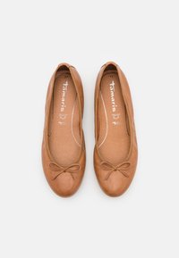 Paire de ballerines en cuir marron clair avec bouts ronds et petits nœuds en décoration, vues de dessus sur un fond blanc.
