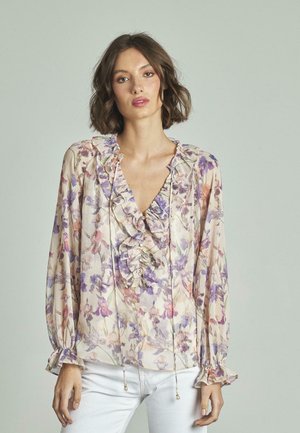 Blouse à manches longues en tissu léger à motifs floraux, avec un col et des poignets à volants, présentant une base crème avec des accents violets et roses.