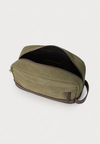 Green canvas bag with a zippered top, featuring a dark brown leather base and side accents. Interior is black with a smooth texture.