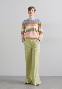 Lightweight sweater with horizontal stripes in orange, beige, green, and blue, paired with high-waisted, wide-leg, light green trousers.