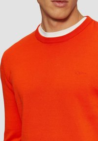 Helle orange Strickjacke mit einem gerippten Rundhalsausschnitt und subtilen Logodetails. Sie hat eine glatte Textur und eine enganliegende Passform.
