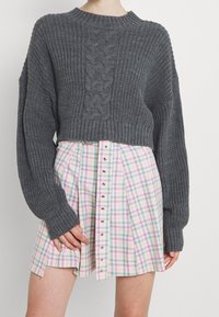 Grauer, kabelgestrickter, kurzer Pullover mit weiten Ärmeln, kombiniert mit einem karierten Minirock in Pastellfarben und mit vorderem Knopfverschluss.