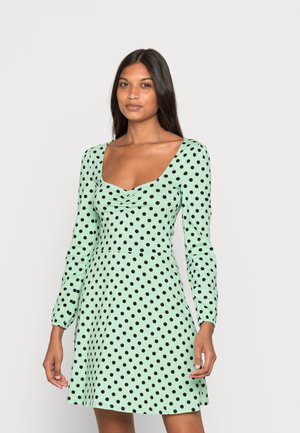 Vestido verde menta com mangas longas, apresentando bolinhas pretas, um decote quadrado e um detalhe franzido na zona do busto. Textura do tecido suave.