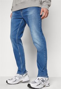 Světle modré džíny ze denimu s bledým lemem, slim fit a klasickým pětikapsovým designem, doplněné o bílé a stříbrné sportovní boty.