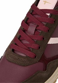 Gros plan d'une basket en cuir bordeaux avec des accents en daim marron foncé et des lacets épais assortis passés dans des œillets.