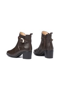 Botas de cuero marrón hasta el tobillo con un acabado brillante, cremallera lateral y correa decorativa con un hebilla de metal. Tacón cuadrado de aproximadamente 2.5 pulgadas.