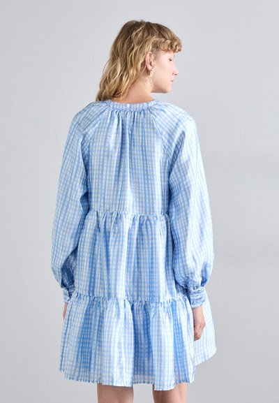 Robe à carreaux bleus et blancs avec une jupe à volants, des manches longues bouffantes et un col froncé. Tissu doux avec une texture légèrement brillante.