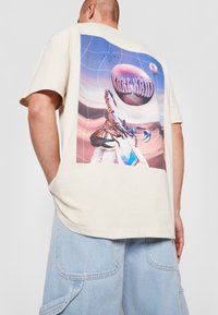 Beige cotton T-shirt featuring a large, colorful graphic of a scorpion on a cosmic background with "KARL KANI" text at the top.