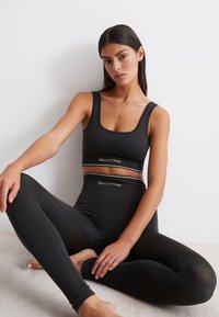 Svart träningsset bestående av en ribbad sport-bh och högmidjade leggings med vita logotypdetaljer. Slät textur, åtsittande design.