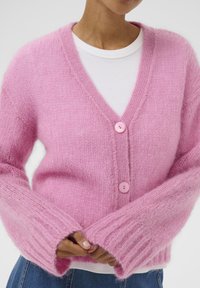 Rosa gestrickte Strickjacke mit V-Ausschnitt, mit breiten, gerippten Ärmeln und zwei rosa Knöpfen. Weiche, flauschige Textur und lockere Passform.