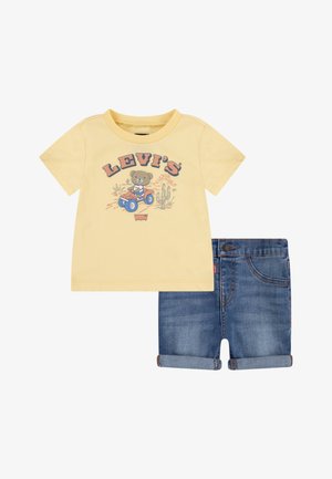 Dzeltena kokvilnas T-kreklis ar lāča grafiku; zili džinsu šorti ar rolētām piedurknēm un piecu kabatu dizainu; ar zīmolu "LEVI'S."
