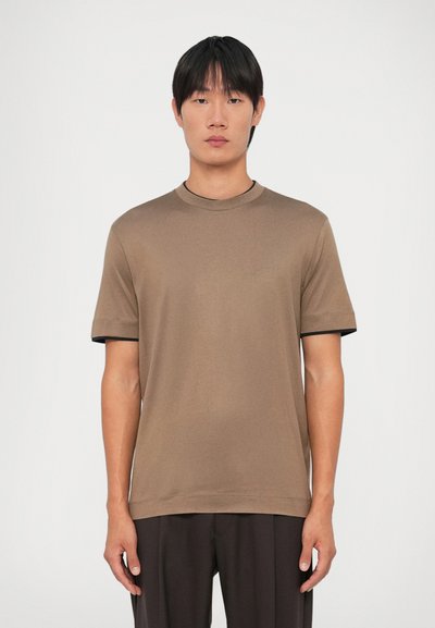Brązowy t-shirt z krótkim rękawem i okrągłym dekoltem, z kontrastowym czarnym wykończeniem rękawów. Wykonany z gładkiego materiału, luźno dopasowany.