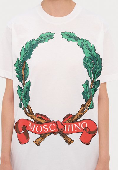 Bílý tričko se grafickým designem zelených listů, hnědých větví a červené stuhy s textem "MOSCHINO" v bílé barvě.