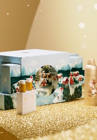 Geschenkset mit einer dekorativen Box, die schneebedeckte Berge und bunte Häuser zeigt. Enthält eine goldene Flasche und zwei weiße Flaschen mit goldenen Akzenten.