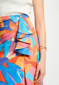 Gonna colorata con un vivace motivo di foglie in blu, arancione e rosa. Presenta un dettaglio di ruches a strati e uno spacco laterale. Tessuto di trama morbida.