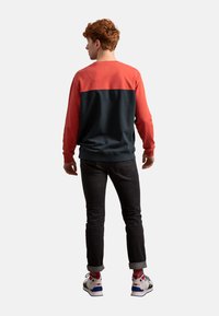 Felpa rossa e blu navy con maniche lunghe e scollo rotondo. Tessuto misto cotone, polsini e orlo a coste. Abbinata a jeans scuri e sneakers multicolori.