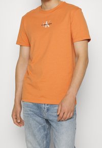 Oranžové bavlněné tričko s kulatým výstřihem a krátkými rukávy, s bílým logem "Calvin Klein Jeans" a standardním střihem.