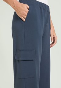 Marineblaue Sporthosen mit glatter Textur, ausgestattet mit einer Seitentasche und einem elastischen Bund, die eine lockere Passform bieten.