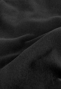 Zwarte katoenen stof met een zachte textuur en zichtbare diagonale weefpatronen, die subtiele lichtreflecties over het oppervlak creëren.