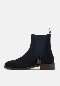 Botte Chelsea en daim noir avec panneau latéral élastique, languette de tirage au talon, petit talon en bois et petite étiquette de marque sur le côté.