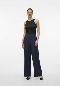 Černý přiléhavý top bez rukávů spárovaný s širokými námořnickými kalhotami s dvojitými knoflíkovými detaily. Model nese černou obuv, minimalistický design, hladká tkanina.