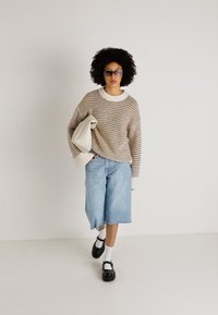 Raidallinen neulepusero beigen, sinisen ja kermaisen sävyissä, yhdistettynä vaaleansinisisiin denimpuku-housuihin. Mustat kengät valkoisilla sukilla. Pitää valkoista laukkua.