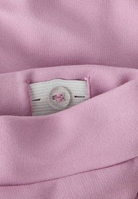 Tejido rosa con una cinturilla elástica ajustable sujeta por un botón, que muestra una fina textura de punto y detalles de costura.