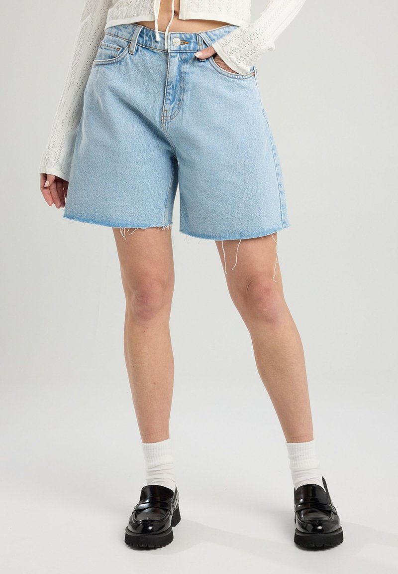 Vaaleansiniset farkkushortsit, joissa on kulutettu helma, viisi taskua ja napitus. Yhdistetty mustiin platform-kengiin ja valkoisiin sukkiin.