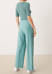 Ljus turkos ribbad stickad topp med korta ärmar, kombinerad med högmidjade, breda byxor i samma färg. Vita sneakers fulländar outfiten.