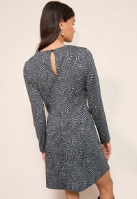 Rochie cu mâneci lungi, cu un model abstract în nuanțe de bleumarin și alb, având o decupare în formă de cheie în spate și o croială lejeră. Textură moale a materialului.