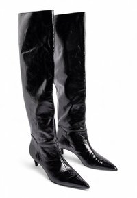 Zem līdz ceļiem melni lakoti ādas zābaki ar paaugstinātu purngalu un mazu papēdi; gluda tekstūra un minimāli šuvju detaļas.