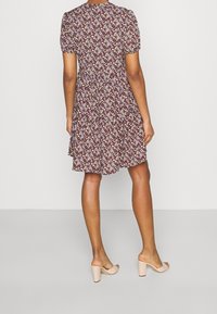 Blumenkleid in Dunkellila mit kurzen Puffärmeln, knielang und mit einem ausgestellten Rock. Kombiniert mit hellrosa Blockabsatz-Mules.