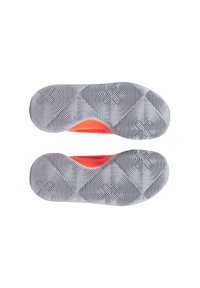 Suelas de zapatillas deportivas con un diseño de goma texturizada en gris, que presenta un patrón circular y acentos en naranja brillante en la zona del mediopié.