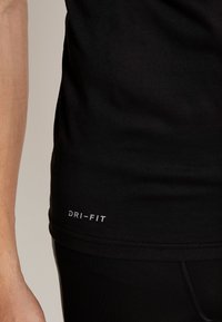 Musta DRI-FIT urheilupaita, jossa on sileä pinta, tiukka istuvuus ja huomaamaton logo helman kohdalla. Suunnittelu mahdollistaa kosteuden siirron.